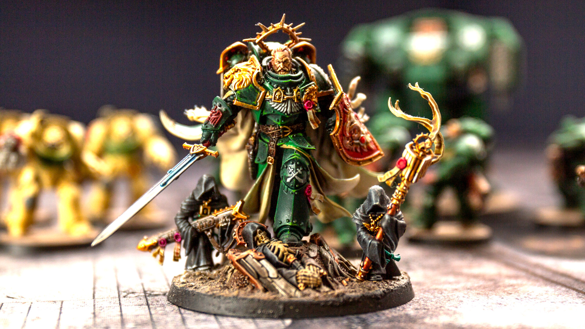 The Lion El'Jonson miniature in green and gold armour, with two small black-hooded Watchers in the Dark crouched on his base carrying his weapons